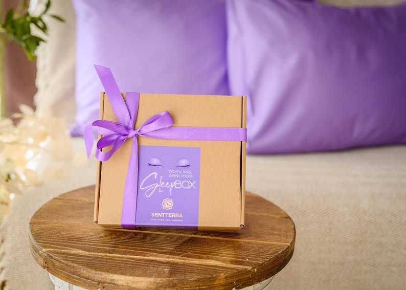 May include: A brown cardboard box with a purple ribbon tied around it. The box has a label that says "Worry less, sleep more SleepBox" and "SENTTERRA".