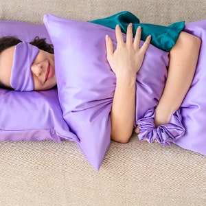 May include: A person sleeping on a purple satin pillow with a sleep mask on their eyes.