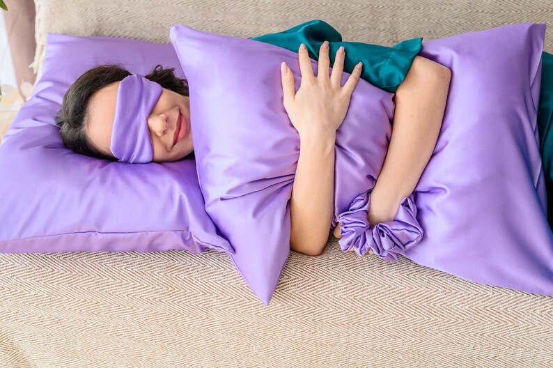 May include: A person sleeping on a purple satin pillow with a sleep mask on their eyes.