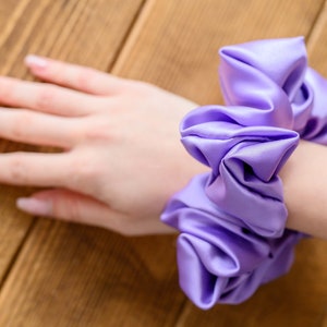 May include: A purple satin scrunchie with a gathered, ruffled design.