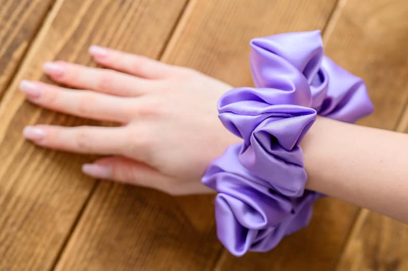 May include: A purple satin scrunchie with a gathered, ruffled design.
