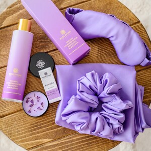 May include: A lavender-themed self-care gift set with a purple satin sleep mask, a satin scrunchie, a bottle of organic lavender water, a small bottle of lavender essential oil, and a lavender candle.