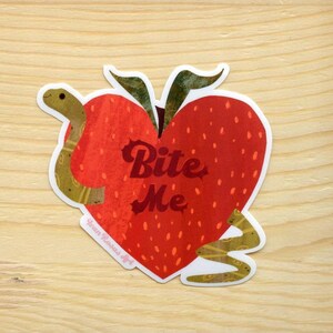 May include: A red heart-shaped strawberry with a green stem and leaves. A brown snake wraps around the strawberry with the text "Bite Me" in a retro font.