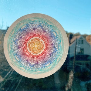 May include: A colorful mandala sticker with a rainbow gradient design. The sticker is on a window with a blurry background.
