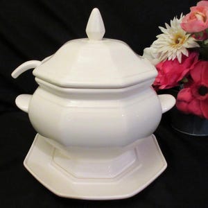 May include: White porcelain soup tureen with a lid and a ladle. The tureen has an octagonal shape and sits on a matching octagonal plate.
