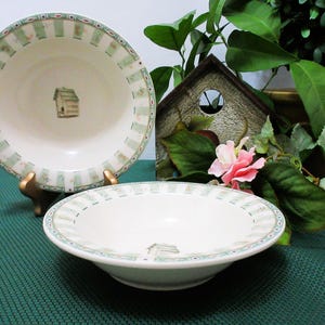 May include: Three white ceramic bowls with a green and beige border design. Each bowl features a small birdhouse illustration in the centre. The bowls are on a green surface, with a decorative birdhouse and flowers in the background.