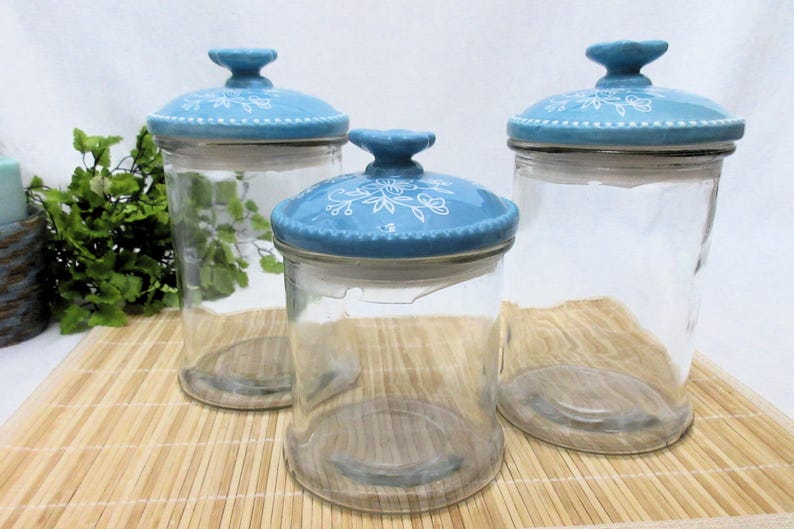 May include: Three glass canisters with blue and white ceramic lids. The lids have a floral design.