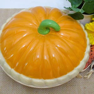 以下が含まれることがあります： 光沢のあるオレンジ色の仕上げと緑色の茎が付いた、カボチャ型のセラミック製サービングディッシュ。 ディッシュはクリーム色のトリムが付いたスカラップエッジです。 秋の季節の装飾品です。