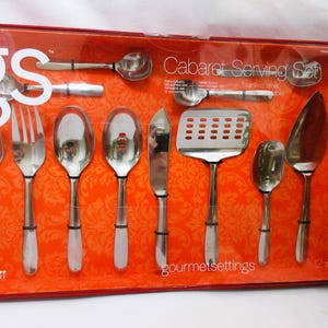 May include: A 12-piece stainless steel Cabaret Serving Set by gourmetsettings in a rectangular orange box. The set includes various spoons, forks, a slotted turner, a spreader, and a server, all secured against a patterned orange background.