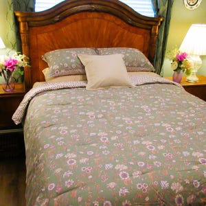 May include: A bedroom with a bed featuring a wooden headboard and matching bedside tables. The bed is made with a green floral patterned duvet cover and pillows. Two lamps with white shades sit on the bedside tables, and vases of flowers add colour.