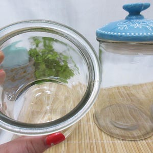 May include: Two clear glass jars with blue and white lids. The lids have a floral design. The jars are empty.
