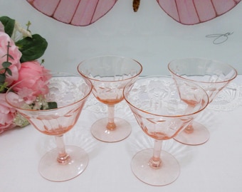 May include: Four vintage pink champagne glasses with etched floral designs. The glasses have a delicate, stemmed base and a wide, shallow bowl. The background includes pink flowers and a decorative butterfly.