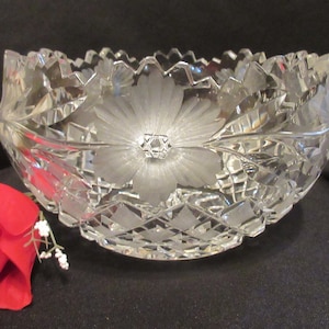 May include: A clear glass bowl with a cut crystal design and a frosted flower pattern. The bowl is round and has a scalloped edge.