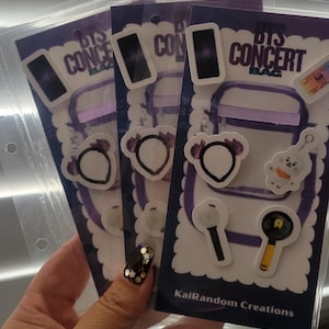 May include: Three packs of BTS Concert Bag stickers. Each pack features a purple background with illustrations of a phone, a bag, a bear, a dog, a microphone, and a fan. The text "BTS CONCERT BAG" and "KaiRandom Creations" are visible.