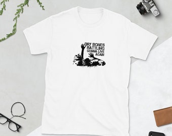 Può includere: Maglietta bianca con una grafica nera di una mano che esce dal terreno con il testo "DRY BONES RATTLING GONNA LIVE AGAIN".