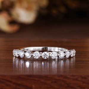 Puede incluir: Una banda plateada delicada con una fila de piedras redondas y transparentes. El anillo está sobre una superficie de madera.