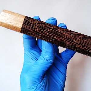 May include: A wooden cylinder with a dark brown wood grain and a light brown top. The cylinder is approximately 15 cm long and 4 cm in diameter.