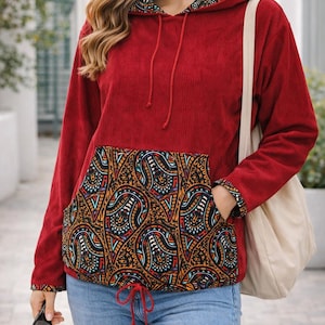 Peut inclure: Un sweat à capuche en velours côtelé rouge avec une poche et une doublure de capuche à motifs. La poche et la doublure de la capuche présentent un motif cachemire coloré avec des accents orange, bleu et noir. Le sweat à capuche a un cordon de serrage et des manches longues.