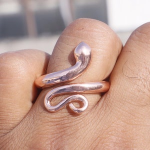 Puede incluir: Un anillo de serpiente de oro rosa con un diseño en espiral. El anillo se lleva en un dedo.