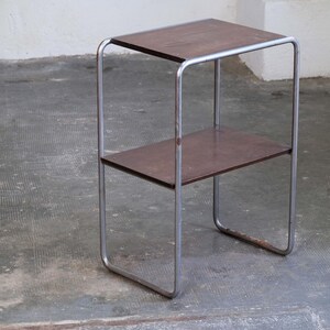 May include: A small, two-tiered side table with a dark brown wooden top and shelf. The frame is made of silver-colored metal. The table has a minimalist design and is suitable for various uses.