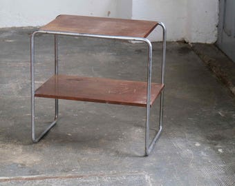May include: A small, two-tiered side table with a dark brown wooden top and shelf. The frame is made of silver-colored metal. The table is approximately 24 inches long, 12 inches wide, and 20 inches tall.