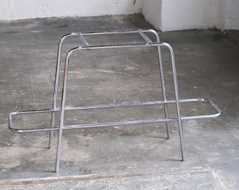 May include: A chrome metal plant stand with two shelves. The stand has a simple, geometric design.