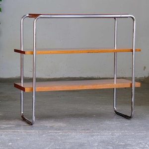 Può includere: Una mensola a tre livelli con struttura cromata e ripiani in legno. I ripiani sono di colore marrone chiaro e la struttura ha un design curvo. L'unità è autoportante e sembra essere vintage.
