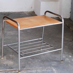 May include: A chrome metal side table with a wooden top and a lower shelf. The table has a simple, modern design.