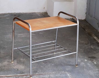 May include: A chrome metal side table with a wooden top and a lower shelf. The table has a simple, modern design.