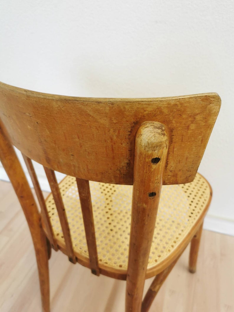 May include: A wooden chair with a curved back and a woven cane seat. The chair is made of light brown wood and has a simple, classic design.