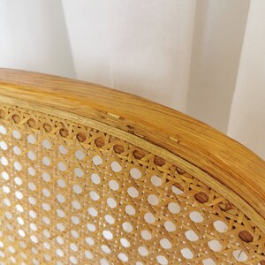 May include: Close-up of a woven cane chair seat with a natural wood frame. The cane is woven in a tight pattern, creating a smooth and durable surface.