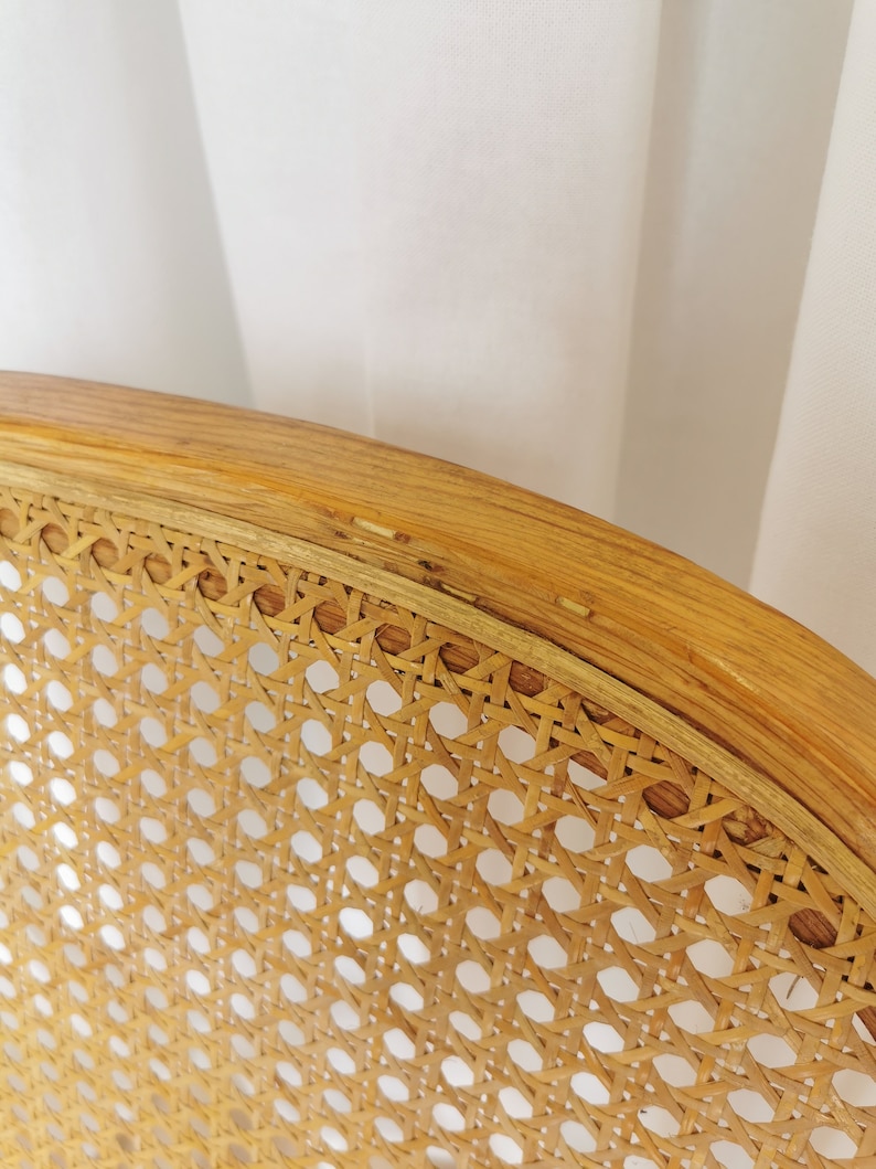 May include: Close-up of a woven cane chair seat with a natural wood frame. The cane is woven in a tight pattern, creating a smooth and durable surface.