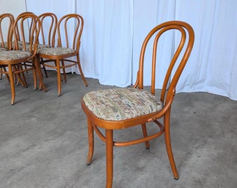 May include: A set of bentwood chairs featuring a warm brown wood finish and curved backrests. Each chair has a padded seat upholstered in a light-colored fabric with a multi-colored patterned design. The chairs have four legs and a circular frame.