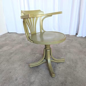 May include: A vintage olive green desk chair with a curved back and a small writing surface. The chair has a round seat and a pedestal base. The chair is made of wood and has a glossy finish.