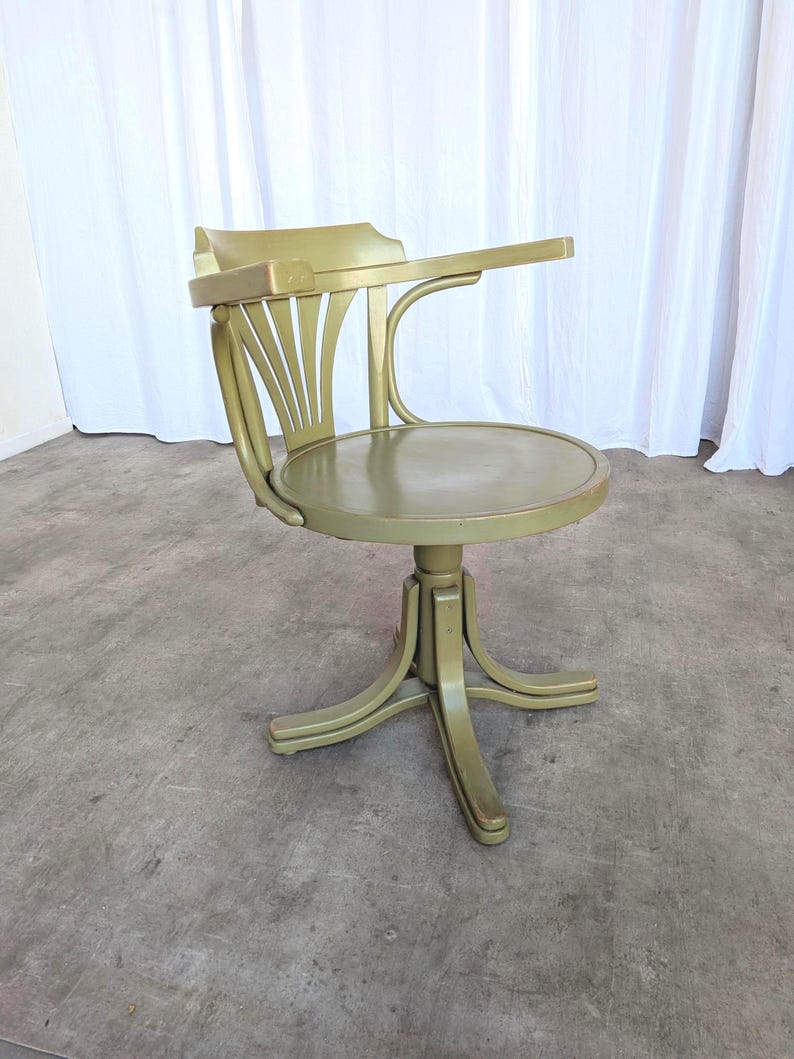May include: A vintage olive green desk chair with a curved back and a small writing surface. The chair has a round seat and a pedestal base. The chair is made of wood and has a glossy finish.