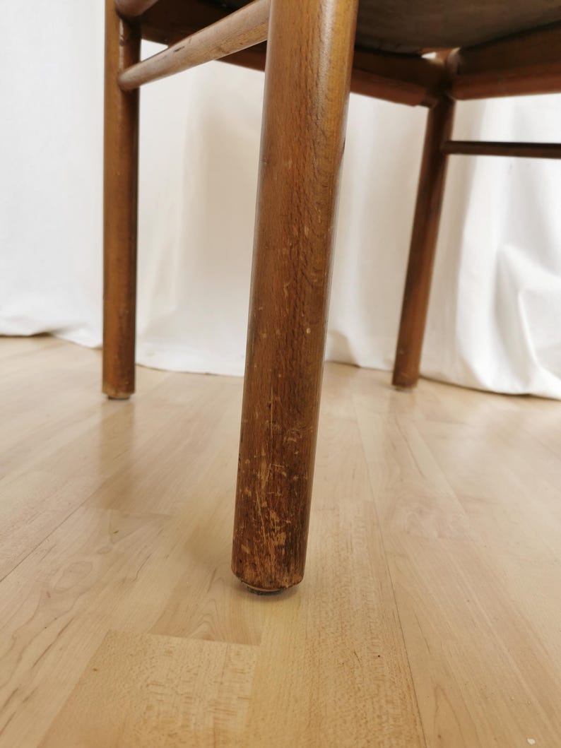 May include: Close-up of the wooden leg of a chair. The leg is brown and has a worn finish. The chair is sitting on a light wood floor.