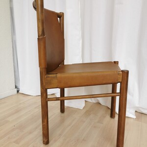 May include: A brown leather chair with a wooden frame. The chair has a simple design with a rectangular seat and back.
