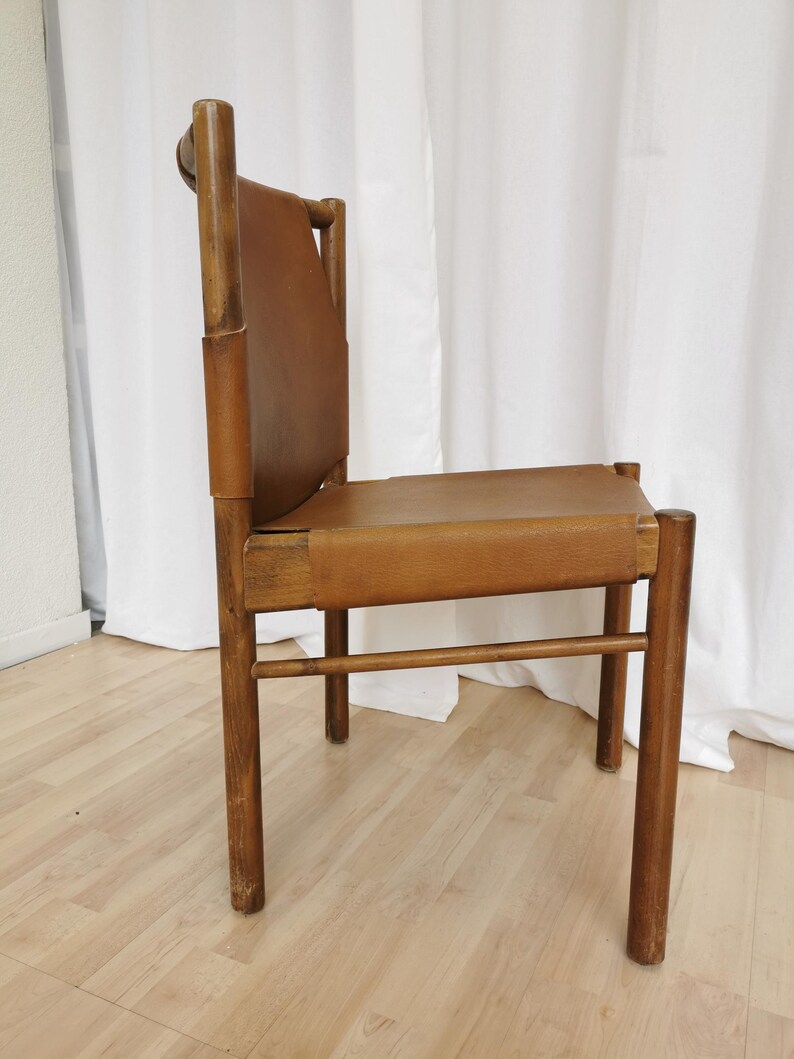 May include: A brown leather chair with a wooden frame. The chair has a simple design with a rectangular seat and back.
