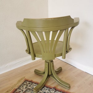 May include: A vintage olive green swivel chair with a curved back and a round seat. The chair has a star-shaped base and is positioned in a corner. The chair is made of wood and has a distressed finish.