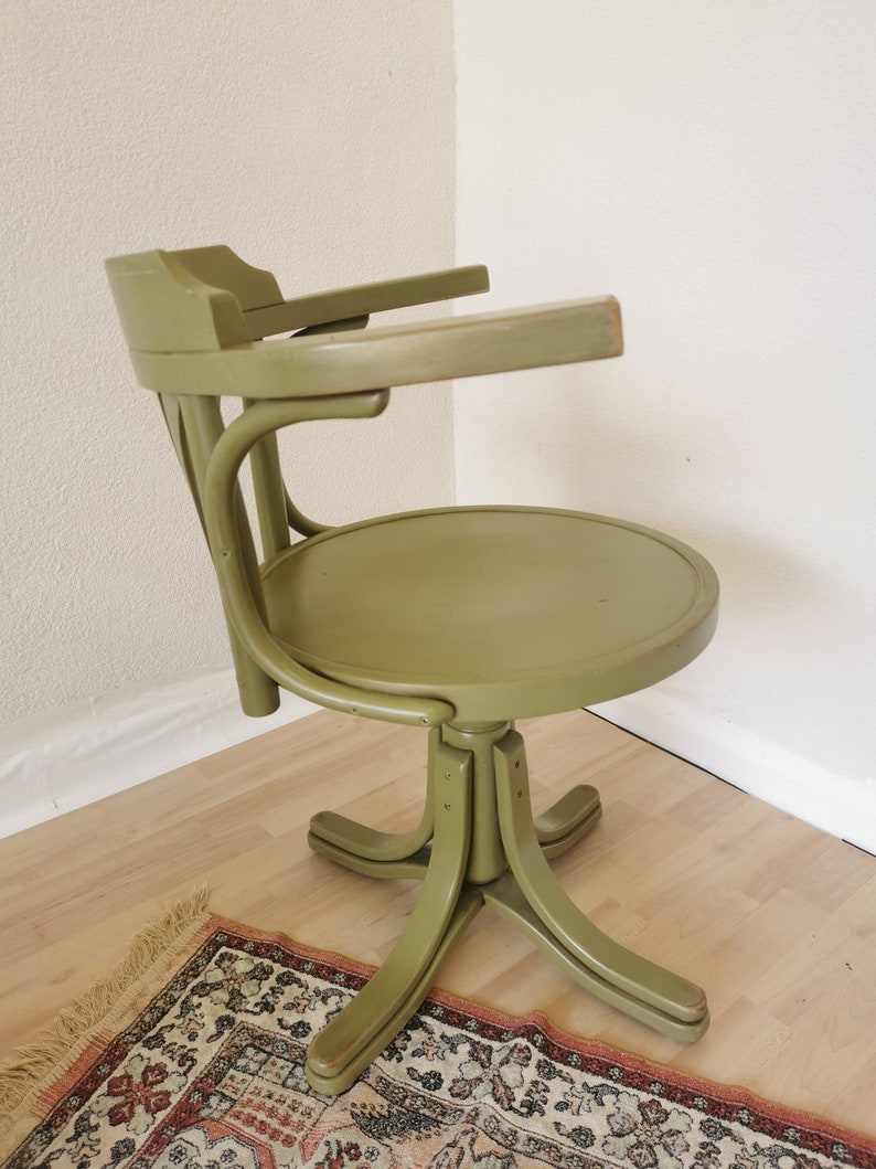 May include: An olive green vintage office chair with a round seat and curved back. The chair has armrests and a five-point base. The chair is made of wood and has a swivel function.