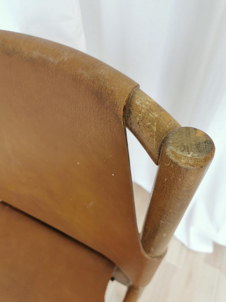May include: Close-up of a brown leather chair with wooden arms and a wooden back. The chair is in good condition, with some wear and tear on the leather.