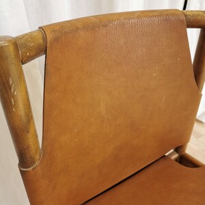 May include: A brown leather chair with a wooden frame. The chair has a high back and a wide seat.