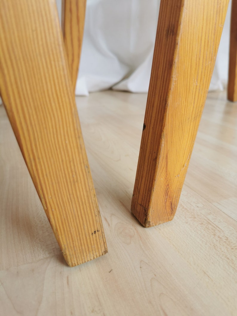 May include: Close-up of the legs of a wooden chair. The legs are made of light-colored wood and have a simple, straight design.