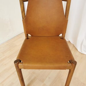 May include: A brown leather chair with a wooden frame. The chair has a simple design with a rectangular seat and back.