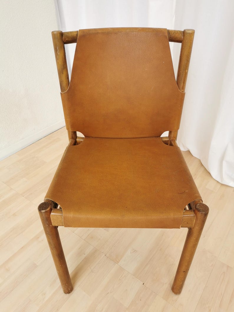 May include: A brown leather chair with a wooden frame. The chair has a simple design with a rectangular seat and back.