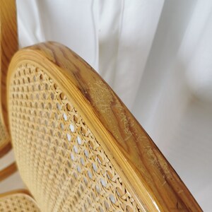 May include: Close-up of a wooden chair with a woven cane seat and back. The chair is made of light brown wood and has a natural finish. The cane is woven in a tight pattern and is in good condition.