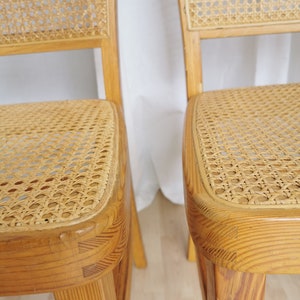 May include: Two wooden chairs with cane seats. The chairs are light brown and have a simple design.