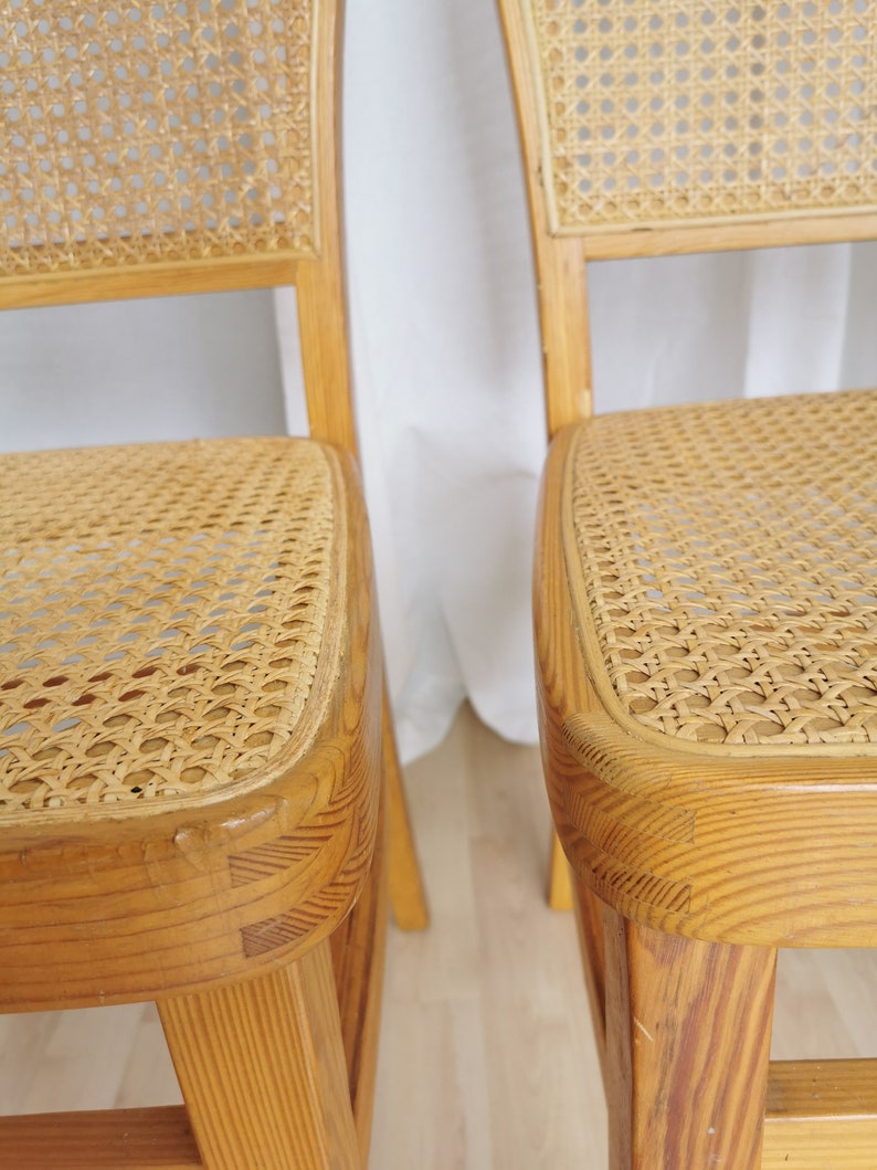 May include: Two wooden chairs with cane seats. The chairs are light brown and have a simple design.