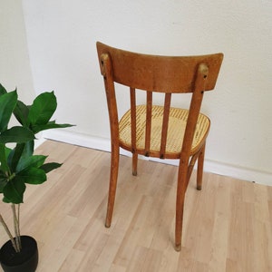 May include: A wooden chair with a woven cane seat and a curved back. The chair is light brown in color and has a simple design.