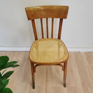 May include: A wooden chair with a woven cane seat. The chair has a simple design with a curved back and four legs.